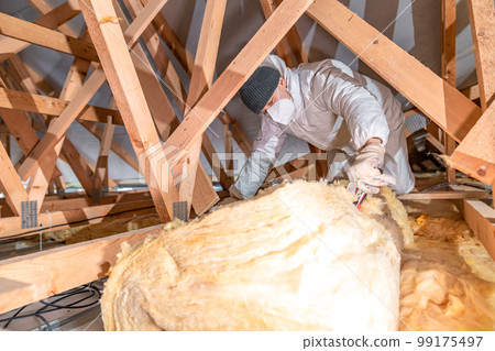 man insulates the roof and ceiling of the house with glass wool man insulates the roof and ceiling of the house with glass wool 99175497