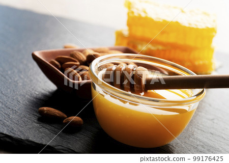 Slate tray with honey almonds and honeycomb on kitchen table 99176425