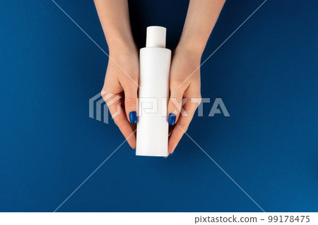 Female hands holding cosmetics container in hands against blue background 99178475