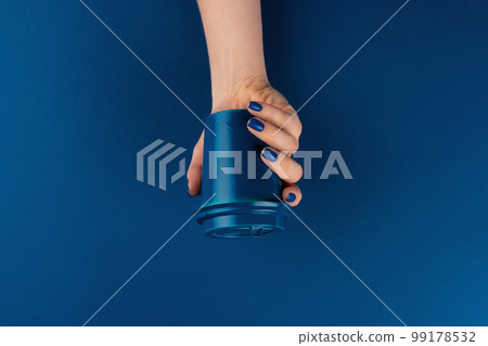 Female hand holding takeaway coffee cup gainst classic blue background Female hand holding takeaway coffee cup gainst classic blue background 99178532
