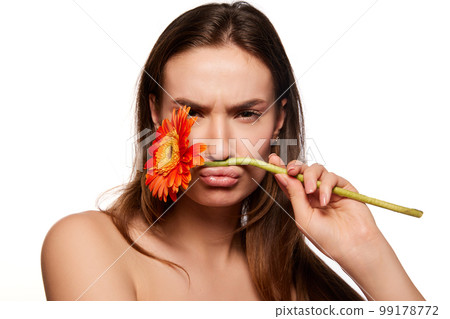 Beautiful young girl with well-kept clean skin posing with gerbera flower over white studio background. Anti-wrinkle care with organic cosmetics Beautiful young girl with well-kept clean skin posing with gerbera flower over white studio background. Anti-wrinkle care with organic cosmetics 99178772