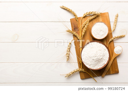 Flat lay of Wheat flour in wooden bowl with wheat spikelets on colored background. world wheat crisis Flat lay of Wheat flour in wooden bowl with wheat spikelets on colored background. world wheat crisis 99180724