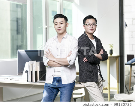 two young asian entrepreneurs standing in office looking at camera with arms crossed 99180725