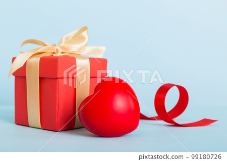 gift box with red bow and red heart on colored background. Perspective view. Flat lay gift box with red bow and red heart on colored background. Perspective view. Flat lay 99180726