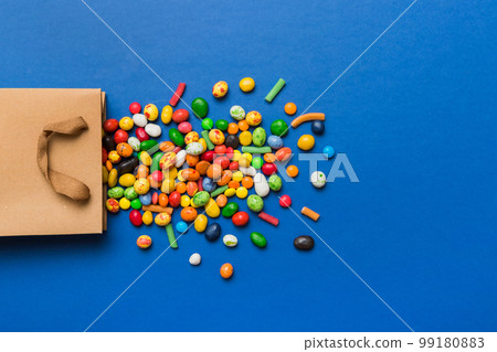 shopping paper gift bag in corner full of assorted traditional candies falling out on colored background with copy space. Happy Holidays sale concept 99180883