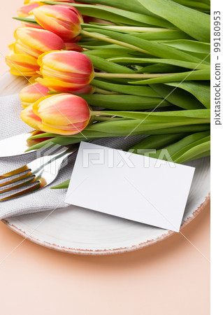 Festive table setting with a card and bouquet of tulips on a beige background. Mockup Festive table setting with a card and bouquet of tulips on a beige background. Mockup 99180953