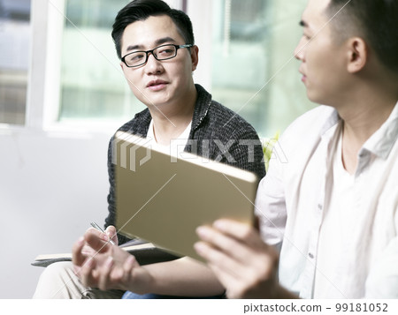 two young asian entrepreneurs discussing business in office using digital tablet 99181052