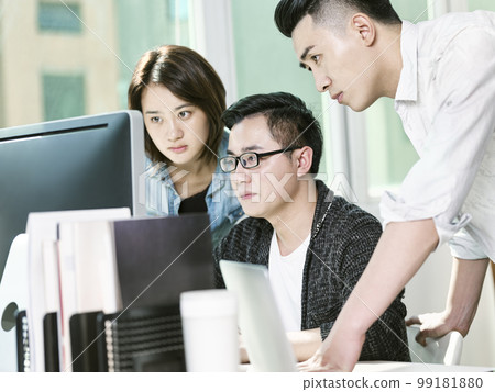 team of three young entrepreneurs analyzing data in office using desktop computer 99181880