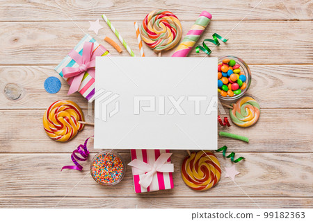 Flat lay holiday composition. Paper blank, lollipop, birthday decorations on Colored background. Top view, copy space for text 99182363