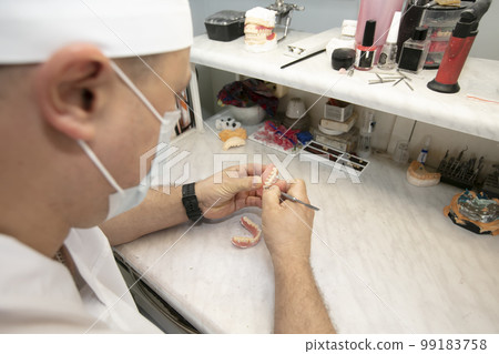 Manufacturing of dentures. Orthopedist's hands make jaw prostheses. 99183758