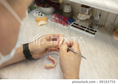 Manufacturing of dentures. Orthopedist's hands make jaw prostheses. 99183759