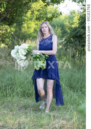An elderly woman, beautiful and well-groomed, walks in the garden with a bouquet of flowers. An elderly woman, beautiful and well-groomed, walks in the garden with a bouquet of flowers. 99183768