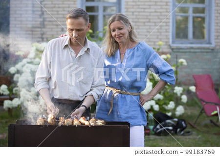 An elderly couple, a man and a woman, are preparing a barbecue. 99183769