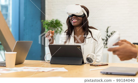 An excited black woman exploring virtual reality in an office An excited black woman exploring virtual reality in an office 99184040