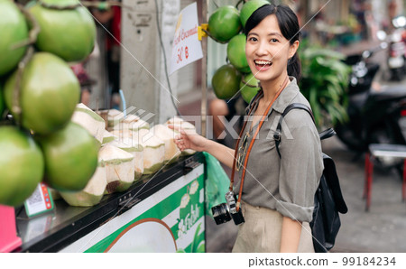 Happy young Asian woman backpack traveler stand in front of coconut juice shop at China town street food market in Bangkok, Thailand. Traveler checking out side streets. 99184234