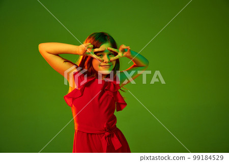 Positive vibe, good mood. Little girl, child in red outfit posing over green studio background in neon light. Concept of childhood and emotions Positive vibe, good mood. Little girl, child in red outfit posing over green studio background in neon light. Concept of childhood and emotions 99184529