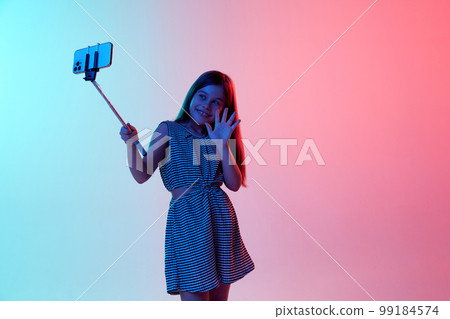 Little beautiful girl, child having video call on phone over gradient blue pink studio background in neon light. Concept of emotions and childhood 99184574