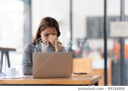 Young businesswoman working on laptop stressed has a headache and thinks hard from work at the office Young businesswoman working on laptop stressed has a headache and thinks hard from work at the office 99184866