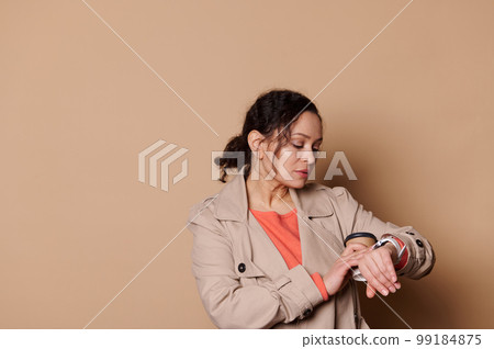 Confident woman entrepreneur checking time on her wrist watch, harrying up for a meeting, isolated on beige background Confident woman entrepreneur checking time on her wrist watch, harrying up for a meeting, isolated on beige background 99184875