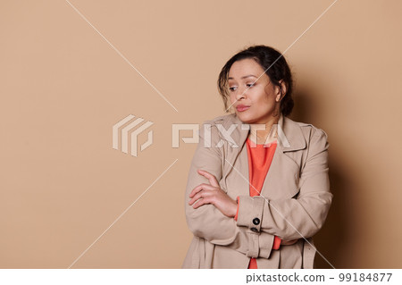 Unsure woman with folded hands looks away, apprehensive, expressing insecurity and worry over beige background. Ad space Unsure woman with folded hands looks away, apprehensive, expressing insecurity and worry over beige background. Ad space 99184877