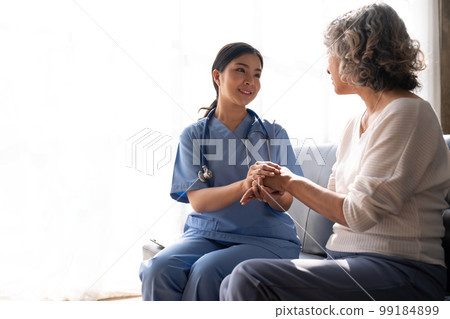 Young female physician giving hope forward to smiling elderly lady patient holding her hand in palms 99184899