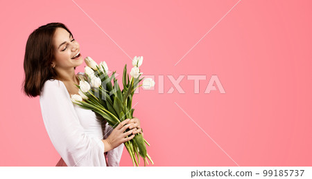 Glad young european woman smelling bouquet of flowers, enjoy lifestyle and aroma of white tulips 99185737