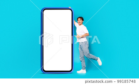 Chinese Teen Guy Pointing Finger At Huge Smartphone, Blue Background 99185748