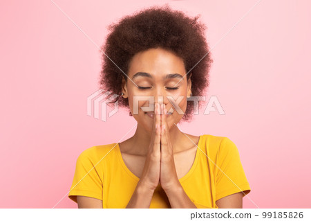 Portrait of happy young black curly lady with closed eyes meditating, praying with hands Portrait of happy young black curly lady with closed eyes meditating, praying with hands 99185826