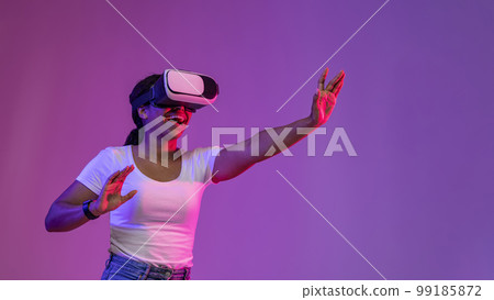 Cheerful Black Female Experiencing Virtual Reality In Vr Glasses Under Neon Lighting Cheerful Black Female Experiencing Virtual Reality In Vr Glasses Under Neon Lighting 99185872
