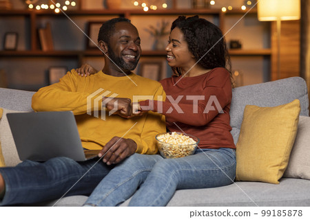 Joyful black couple sitting on couch, using laptop, gambling online 99185878
