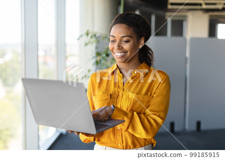 Successful african american businesswoman with laptop in hands standing near window in office interior, copy space Successful african american businesswoman with laptop in hands standing near window in office interior, copy space 99185915