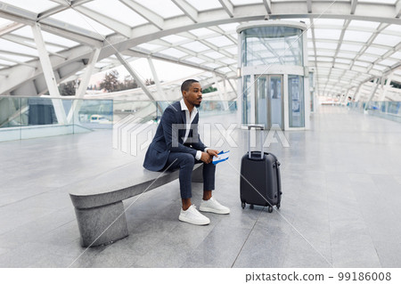 Portrait Of Pensive Young Black Businessman Sitting On Bench At Airport 99186008