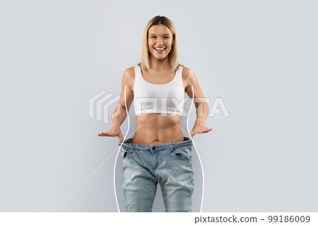 Emotional happy woman in big jeans over grey background 99186009