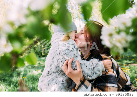 Young woman with her daughter in nature admires white flowering of spring trees Young woman with her daughter in nature admires white flowering of spring trees 99186082