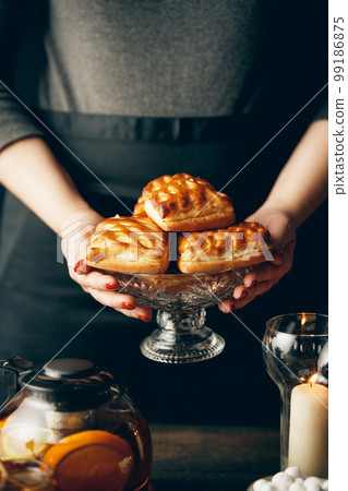 Female baker holding homemade pastries put it on beautifully served table Female baker holding homemade pastries put it on beautifully served table 99186875