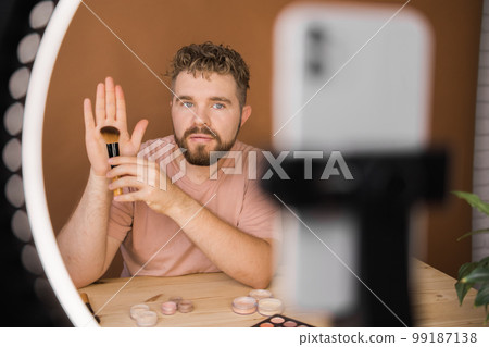 Male beauty blogger with makeup product recording video at home. Using ring lamp and smartphone. Vlog cosmetic products and diversity concept 99187138