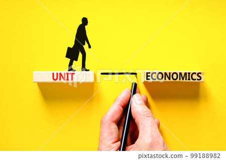 Unit economics symbol. Concept words Unit economics on wooden blocks. Beautiful yellow table yellow background. Businessman hand. Businessman icon. Business and unit economics concept. Copy space. 99188982