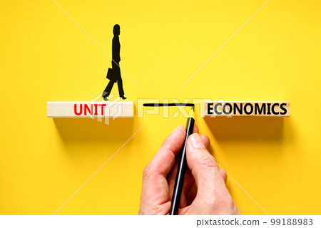 Unit economics symbol. Concept words Unit economics on wooden blocks. Beautiful yellow table yellow background. Businessman hand. Businesswoman icon. Business and unit economics concept. Copy space. 99188983