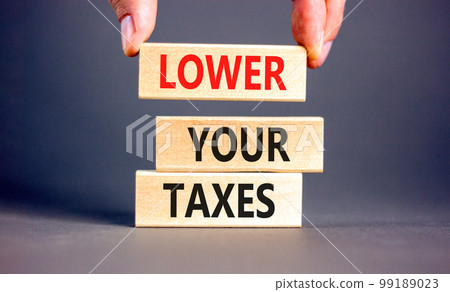 Lower your taxes symbol. Concept words Lower your taxes on wooden blocks on a beautiful grey table grey background. Businessman hand. Business tax lower your taxes concept. Copy space. 99189023