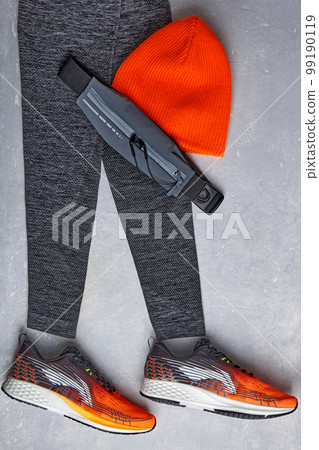 An orange knitted warm hat, warm sports leggings, a fanny pack with headphones and orange sneakers on a light concrete background An orange knitted warm hat, warm sports leggings, a fanny pack with headphones and orange sneakers on a light concrete background 99190119