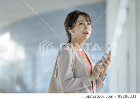 A business woman in her 30s with earphones and a smartphone 99190331