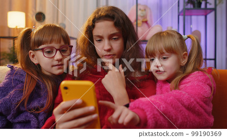 Three siblings children girls using smartphone texting messages on social media applications online 99190369
