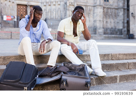 Two frustrated african american travelers sitting with empty suitcases Two frustrated african american travelers sitting with empty suitcases 99193639