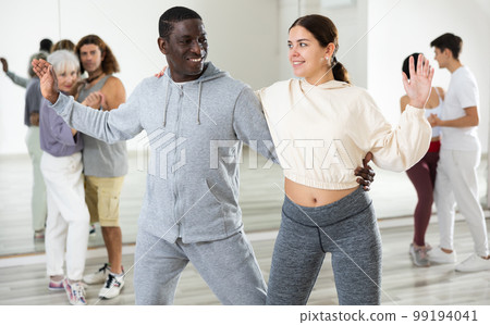 Happy african-american guy and caucasian girl practising paired latin dance in dance studio Happy african-american guy and caucasian girl practising paired latin dance in dance studio 99194041