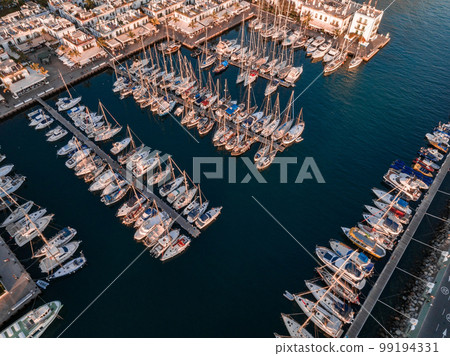 Luxury yachts docked by the golden coast of Spain during magical sunset lights. Luxury holiday concept. Aerial view. Luxury yachts docked by the golden coast of Spain during magical sunset lights. Luxury holiday concept. Aerial view. 99194331