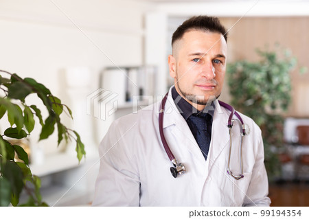 Portrait of friendly male doctor in white coat at clinic Portrait of friendly male doctor in white coat at clinic 99194354