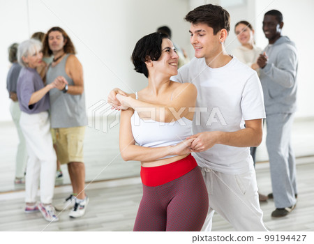 Happy caucasian guy and girl practising paired latin dance in dance studio 99194427