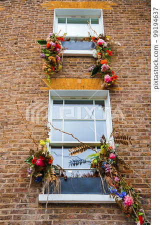 Low angle view of beautiful colorful flowers and leaves decorated on windows of old residential building with brick wall in London Low angle view of beautiful colorful flowers and leaves decorated on windows of old residential building with brick wall in London 99194637