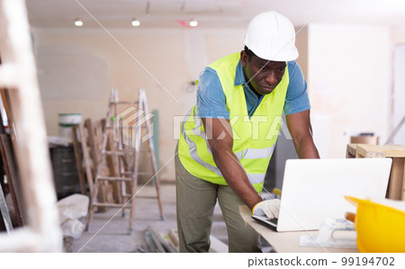 Male worker in yellow vest who checks the work done using laptop 99194702
