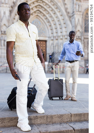 African american traveler strolling with luggage along city street 99194764